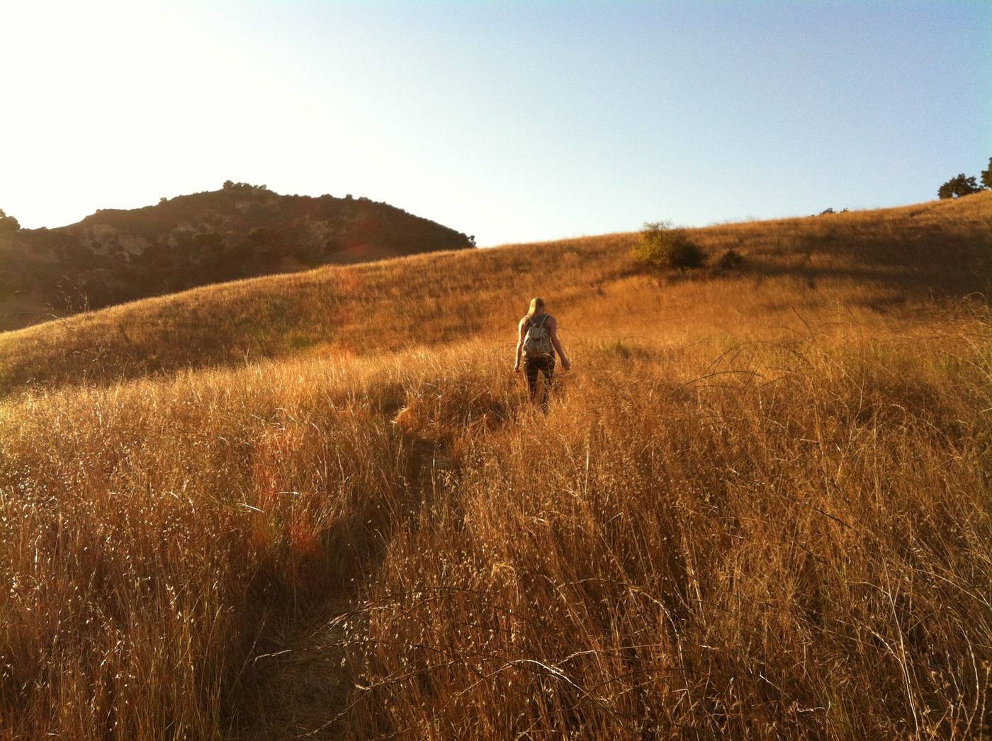 Woman with a backpack walking alone along an open sunlit path under a wide sky