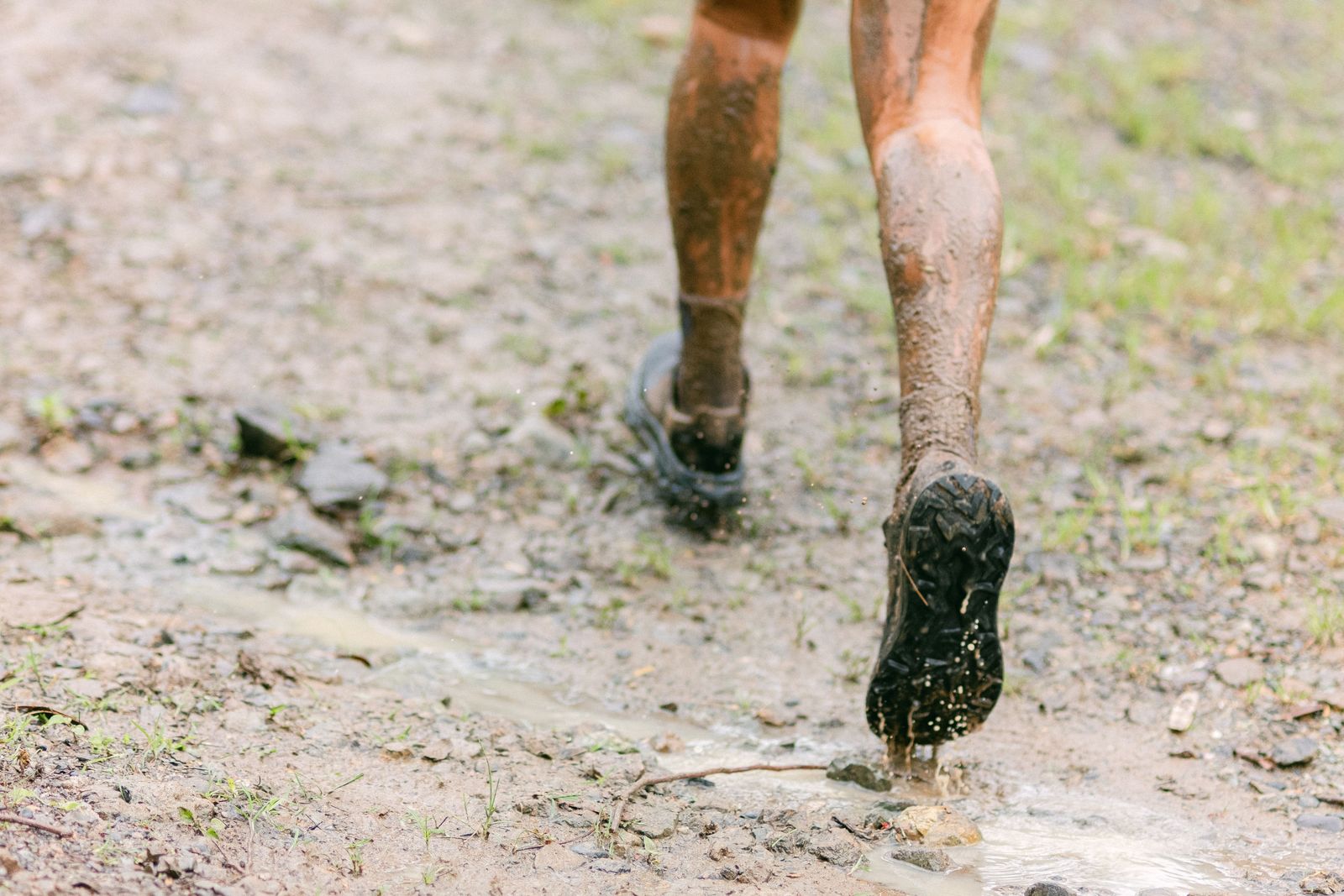 Close-up of trail-running shoes splashing along a wet muddy path
